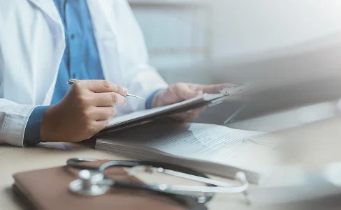 Doctor in a white coat reviewing medical documents with a stethoscope on the table.